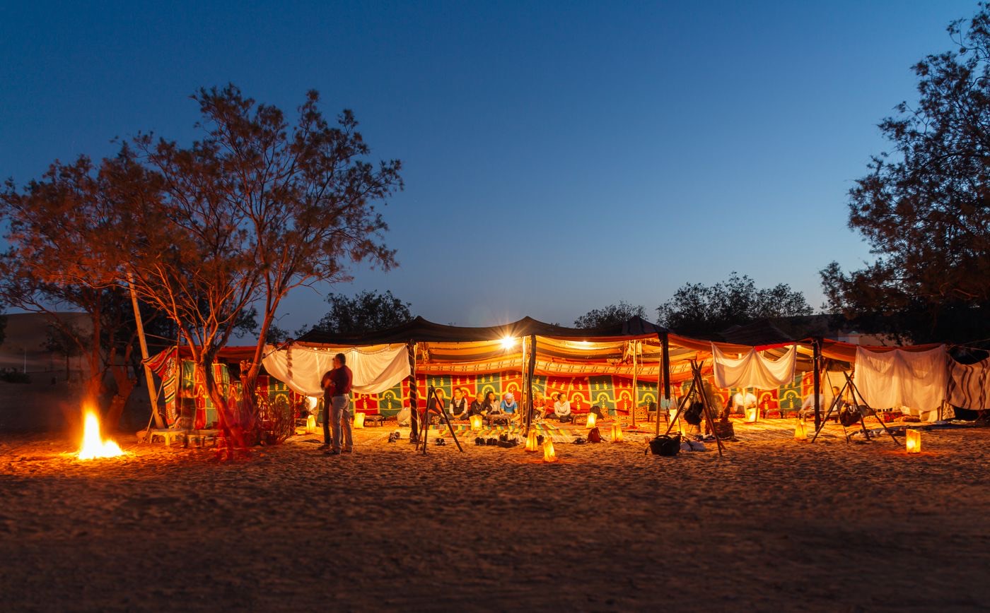 Desert camp with tents and lanterns at dusk